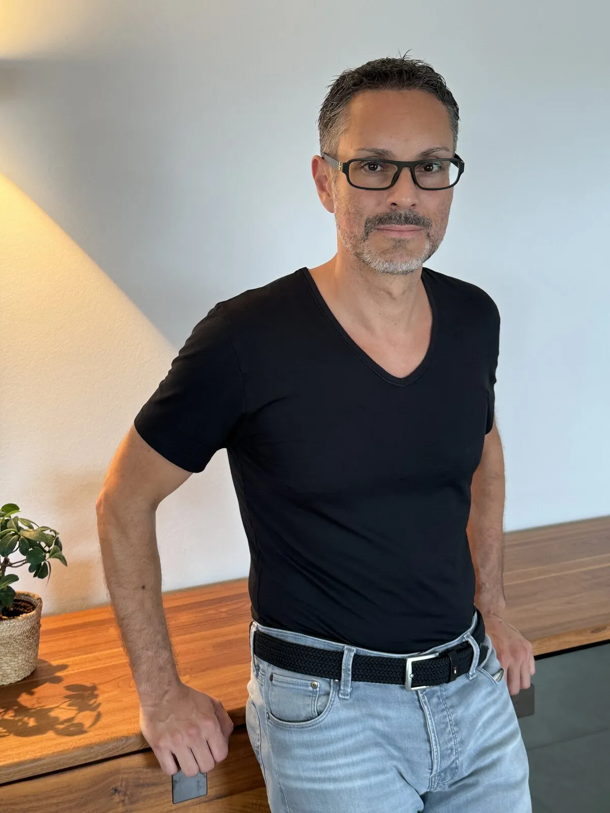 Patrick Schmid steht ruhig an einem Holztisch und schaut zugewandt in die Kamera.
